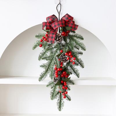 Ziemassvētku asaras formas vītne Mākslīga priežu zara asaras formas vītne ar priedes čiekuru, sarkanām ogām un rūtainu bantīti ziemas priekšdurvīm, sienai, kāpnēm