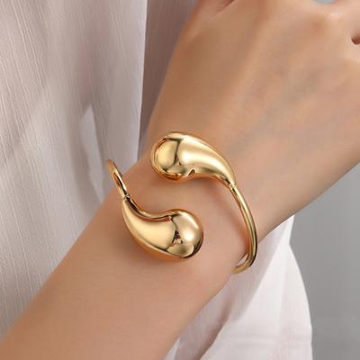Offenes Armband aus Edelstahl mit hohlem, glänzendem Tropfenmuster und Federdraht aus Titanstahl und Gold
