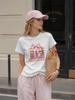 A stylish and versatile white T-shirt with pink book and bow-themed details, perfect for a sophisticated summer look.