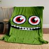 A green face with large red eyes and a wide, toothy grin. for all seasons blanket lunch break throw gift