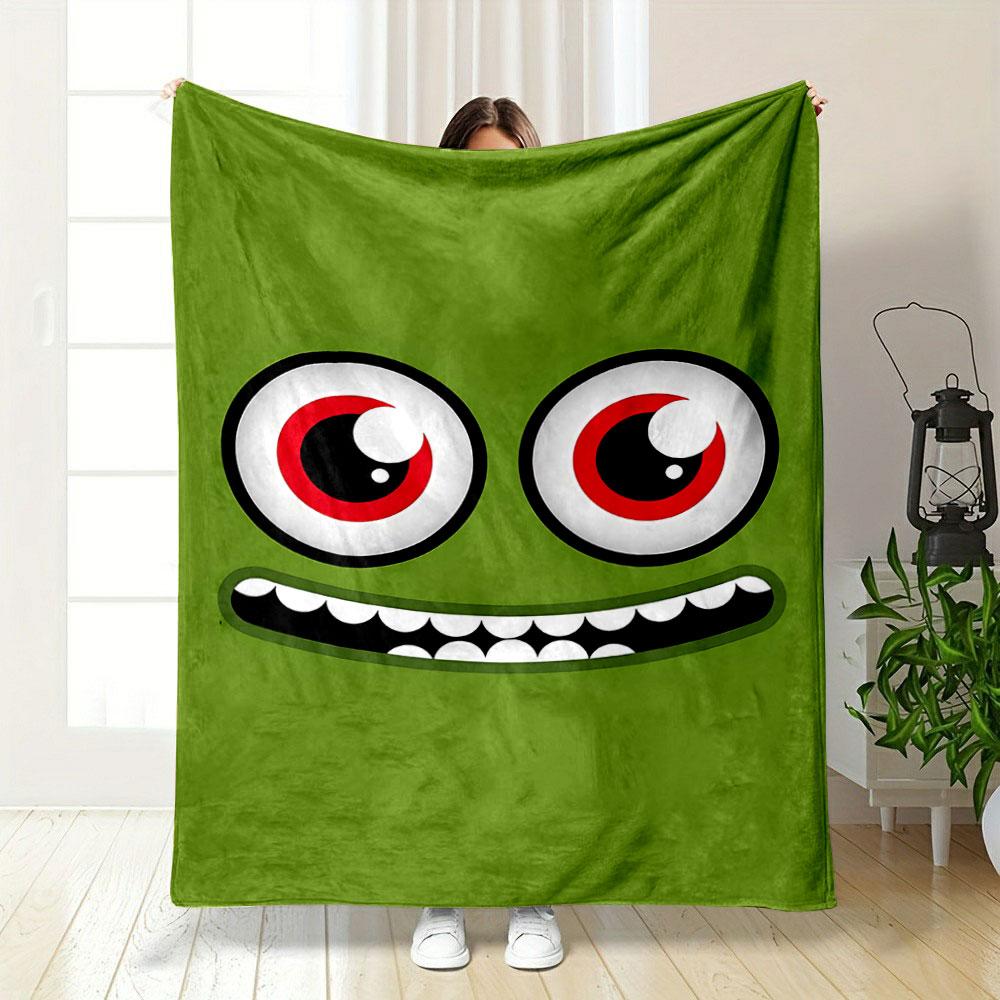 A green face with large red eyes and a wide, toothy grin. for all seasons blanket lunch break throw gift