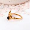 Ornate Black Onyx Crown Ring: Gold-toned jewelry with a round black cabochon and a delicate lotus or tiara-style setting.