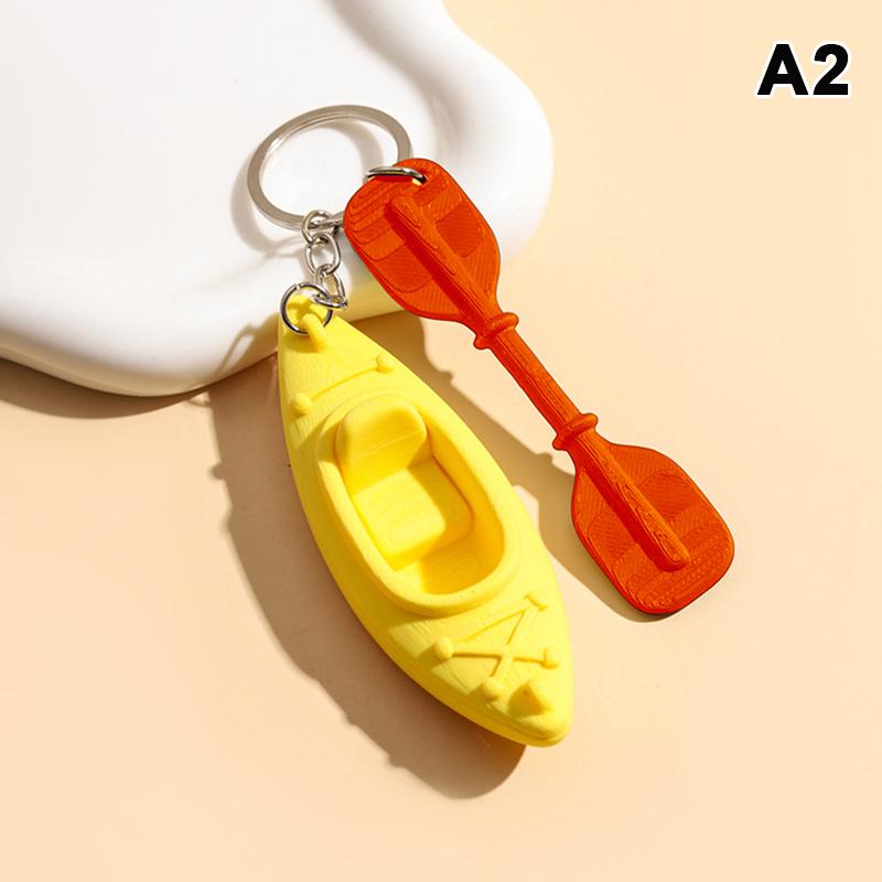 Mini breloczek do kluczy w kształcie kajaka z pasującym wiosłem i żywym wielokolorowym wzorem. Idealny dla miłośników kajakarstwa, dekoracja plecaka, mały prezent.