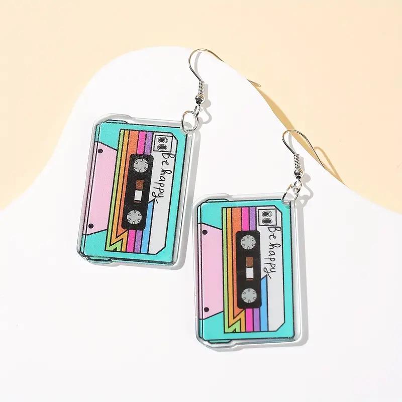 

Пара стильных и минималистичных пластиковых серег-подвесок в виде кассетной ленты, выполненных в минималистичном стиле, идеально подходящих для музыки