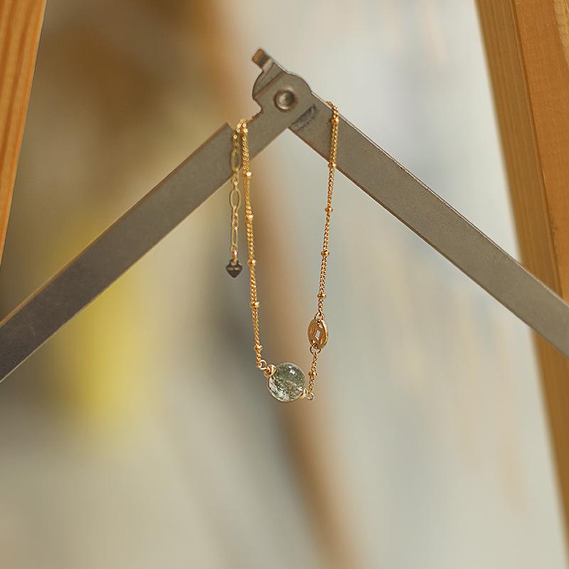 

Женский браслет из натурального золотистого кварца-рутила и зеленого фантомного кварца с бусинами из клубничного кварца с золотым наполнением 14 карат и серого лунного камня