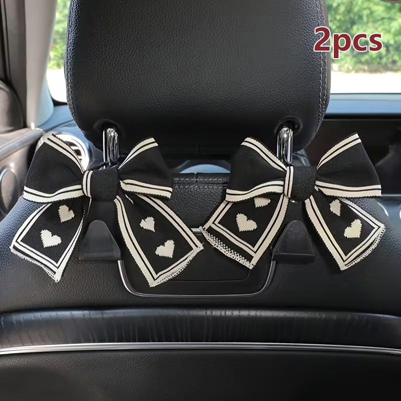 

Two Car Seat Headrest Hooks With A Black And White Heart-shaped Bow Design; Universal Design Suitable For All Vehicles.