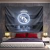 Illuminated Real Madrid crest with crown, displayed above a trophy setup. Patterned tapestry for bedroom and living room home decor