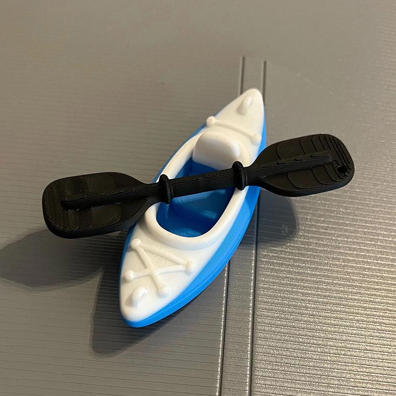 Mini breloczek do kluczy w kształcie kajaka z pasującym wiosłem i żywym wielokolorowym wzorem. Idealny dla miłośników kajakarstwa, dekoracja plecaka, mały prezent.