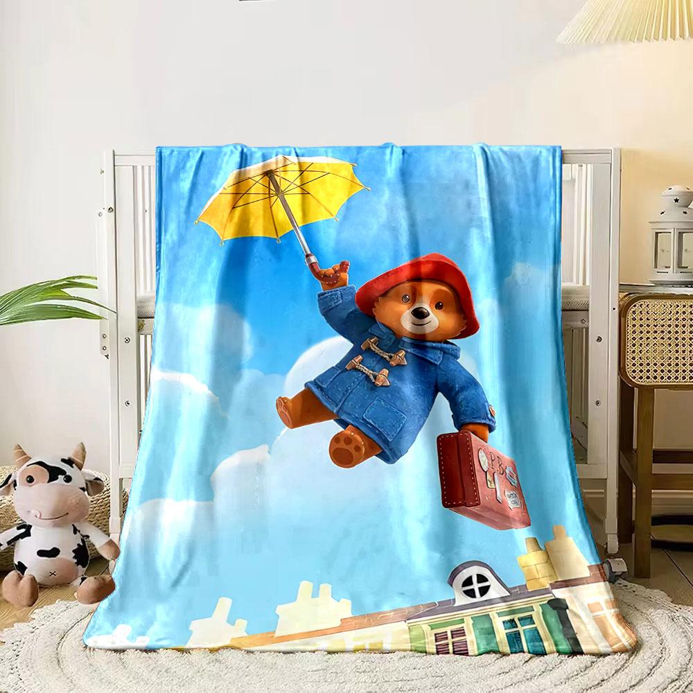 

A bear in a red hood floats with an umbrella and suitcase above houses. for all seasons blanket lunch break throw gift 80cm x 120cm